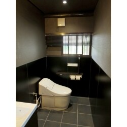 小便器の有った場所を大便器のスペースと一体化して広いトイレに改装しました。床に濃い目のグレーの300角のタイル貼り、トイレはタンクレストイレとし、全体として暗めの落ち着いた空間を提案しました。
壁は腰高までキッチンパネルを貼り、質感もキレイに。専用の手洗いを設け、洗面台上部には洋風なブラケットをつけ、柔らかくあたたかみのある光を加え素敵なトイレになりました。