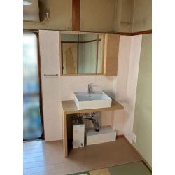 現在、ケアが必要なおばあさまがお住まいで、1階の洗面脱衣所までの動線が長いため2階のお部屋に洗面化粧台を設置したいとのことでした。
洗面化粧台を設置するには給水、給湯、電気のコンセント、排水の確保が必要です。給水と排水はお部屋のベランダに洗濯機置き場があったためそこから取ってクリア。給湯は1階の給湯器が遠い場所に設置されていたため配管を持ってくることができず電気温水器で対応しました。電気温水器の電源は和室の中のブレーカーから取り確保。1つ1つ問題を解決させて、畳をフローリングに交換したら洗面化粧台設置工事の完了です。