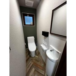 既存はタイル張りの和式トイレで、簡易便座を取り付けて使用されていました。今回はタイル床を解体し、年配のお客様も使いやすいよう床をフラットに施工。壁は既存タイルの上から下地を施工し、クロス仕上げへ変更しました。
内装デザインは複数パターンをご提案し、その中からグリーン系クロスをアクセントにしたデザインを採用。ヘリンボーン柄のクッションフロアも合わせ、店舗の雰囲気になじむ空間に仕上がりました。