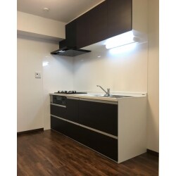 壁付きＩ型キッチン。もともとホワイトを基調としたキッチンでしたが、一新し、スタイリッシュなイメージのキッチンへリフォームしました。収納扉をダークな色を組み合わせることで、すっきりとしたデザインに。床も濃い色のフローリングに張り替え、リビングとの一体感も生まれました。