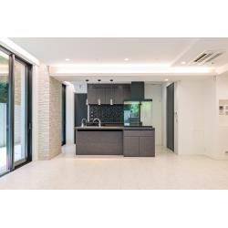 モルタルの無機質な質感に、深い色合いの木目とブラックのアイアンが美しく調和する、都会的で洗練された住まい。
空間の主役は、重厚感のあるモルタル調の腰壁を設えた対面キッチン。背面のオープンシェルフが「見せる収納」として機能し、暮らしに彩りを添えます。あえて梁（はり）をデザインの一部として取り込み、素材の表情を惹き立てることで、ラフさと気品が同居する大人なモダン空間へと生まれ変わりました。