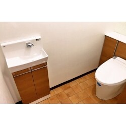 トイレ空間としては広い空間ですが、大便器と小便器があり、大便器側には扉が有る為、広い空間が有効に使われていませんでした。 
今回K様からのご要望で小便器撤去、大便器との仕切壁と扉撤去、手洗器の取替てリフォレの取付を言われました。仕切壁を撤去するのでタイルからクロス・クッションフロアへの改修も行いました。
リフォレを取付けた事で、配管類も綺麗に隠れて見た目がスッキリして広い空間が有効利用出来る様になりました。
明るいクロスと温かみあるテラコッタのクッションフロアとリフォレのキャビネットが、いい感じで温かみのあるトイレ空間になり大変喜ばれました。