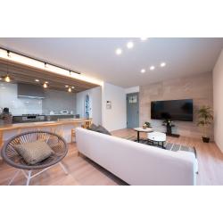 木目の天井や落ち着いたグレーキッチン、アクセントとなるテレビ背面の石目調ウォールが調和した、ナチュラルモダンなLDKへリフォームしました。ダイニングとリビングがゆるやかにつながるレイアウトにより、家族が心地よく過ごせる開放的な空間に。素材感を大切にしたインテリアで、上質であたたかい暮らしを叶えています。