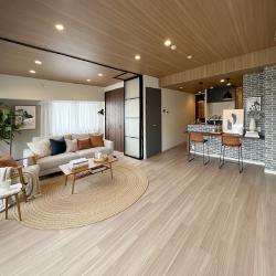 リビングからキッチン、立川ブラインドで仕切られた洋室兼リビングまで、一望できる画角です。床にはナオスフローリング、天井には少し濃いめの板目模様を採用し、高級感と落ち着きを兼ね備えた広々空間に仕上げました。キッチン側のカウンター壁にはレンガ調のアクセントクロスとおしゃれなカウンターを設け、壁のないカウンターキッチンとして演出。コストを抑えつつもデザイン性を大切にした、住まうほどに愛着が深まり、毎日の暮らしが特別に感じられる上質な空間です。