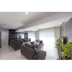 マンション特有の梁による圧迫感に悩んでいたお施主様。その解決のカギは「光の使い方」でした。天井に多灯のダウンライトを配置し、梁の影響を感じさせない明るく開放的な空間に。開口部にはバーチカルブラインドを採用し、隙間から入る光が大理石調の床に反射して、やわらかな光が部屋全体に広がります。さらに垂直のラインを強調することで、天井を高く見せる工夫も。インテリアはアーバンモダンで統一され、建具から家具まで一貫したカラーコーディネートにより、落ち着きと洗練を兼ね備えた空間に仕上がりました。