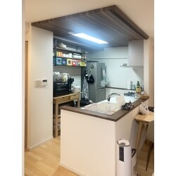 既存の吊戸棚を取り払い、天井に木目のアクセントクロスをご提案。
空間を仕切りつつも圧迫感が無くなり、開放的なキッチンになりました。
カウンター材の塗装をアクセントクロスに合わせた色味にすることで、統一感がある仕上がりになりました。
背面のカップボードには、白煉瓦の壁紙と見せる収納としてウォールシェルフをご提案。
開放的でオシャレなオープンキッチンになりました。