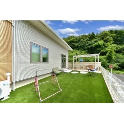 ワンちゃんのドックランとご家族で集まる空間の両方を広く取れるよう、憩いの場としてのテラスを敷地の角に設け、日差しを遮る独立式の屋根と、掃き出し窓の前にテラスへの階段とアプローチを設置。乱形自然石や木調樹脂とホワイトの屋根やフェンスで明るく可愛らしいお庭に。あざやかなグリーンの人工芝は雑草対策にもなります。ワンちゃんの足も洗える大型パンの水栓や、ホースを付けたままにできる補助蛇口、リードを掛けられるフックや収納倉庫など、機能性も抜群のお庭です。