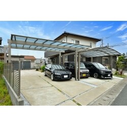 新車を購入されたばかりなのに雪で何回も汚れてしまい、屋根を早急にご希望されてました。既存の屋根との高さや被り、境界ラインが斜めになってる事など、規格外の納まりが難しい条件でしたが、豊富なバリエーションの三協アルミ「スカイリード」を採用し、庭奥の物置まで車を停める事もあるので間口は最大に広げて設置しました。車庫幅最大に広げた事により安心して駐車でき、勝手口までの動線も雨を防ぐ事ができるようになりました。スタイリッシュなフラット屋根デザインでありながら高い強度を確保し、シャイングレーでまとめることで既存屋根やフェンスとも調和のとれた外構となりました。