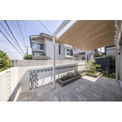 タイルテラスとウォールを施工しました。ウォールには、台形の少しかわったタイル・空洞レンガを入れ抜け感を演出。オーニングは家に固定せず設置できる４本柱。シェードがあるとお庭で過ごす幅がぐっと広がります。吹き抜けになるオーニングと柔らかい印象の素材が集まった素敵なお庭になりました。