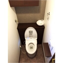 トイレの水漏れが発生しており、これを機に最新のトイレにしたいとのご要望でした。お客様の方でショールームで検討した結果、座り心地の良い商品を選定し、ご依頼頂きました。トイレ背面に設置した棚、天井の収納、手洗い器もセットの商品で、棚の中にタンクが設置されています。機能的ですっきりとした空間に生まれ変わり、お客様より「別世界だね！」との嬉しいお言葉を頂けました。