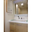 収納豊富な洗面化粧台です。木目調の扉と白を基調とした部屋なので温かみのある空間に仕上がっています。
三面鏡の裏と洗面台の左横に新たに収納棚を設けました。
