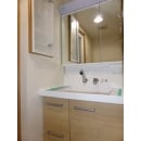 収納豊富な洗面化粧台です。木目調の扉と白を基調とした部屋なので温かみのある空間に仕上がっています。
三面鏡の裏と洗面台の左横に新たに収納棚を設けました。
