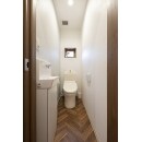 ホワイトを基調とした空間にヘリンボーン柄の床が目を引くデザインに。
木目がアクセントになり、ナチュラルなイメージのトイレ。