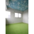 天井には青空の壁紙を張り、床には防音性とふかふかとしたやさしい肌さわりのグリーンのタイルカーペットを敷きました。Ｌ型の窓と相まって爽やかな空間に仕上がりました。