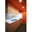 キッチンパネル・リビング側のオーダー家具の天板および取手・開口枠はシルバーのコーディネートで統一させています。壁紙はビタミンカラーのオレンジで、床はフロアタイルのプランニング。