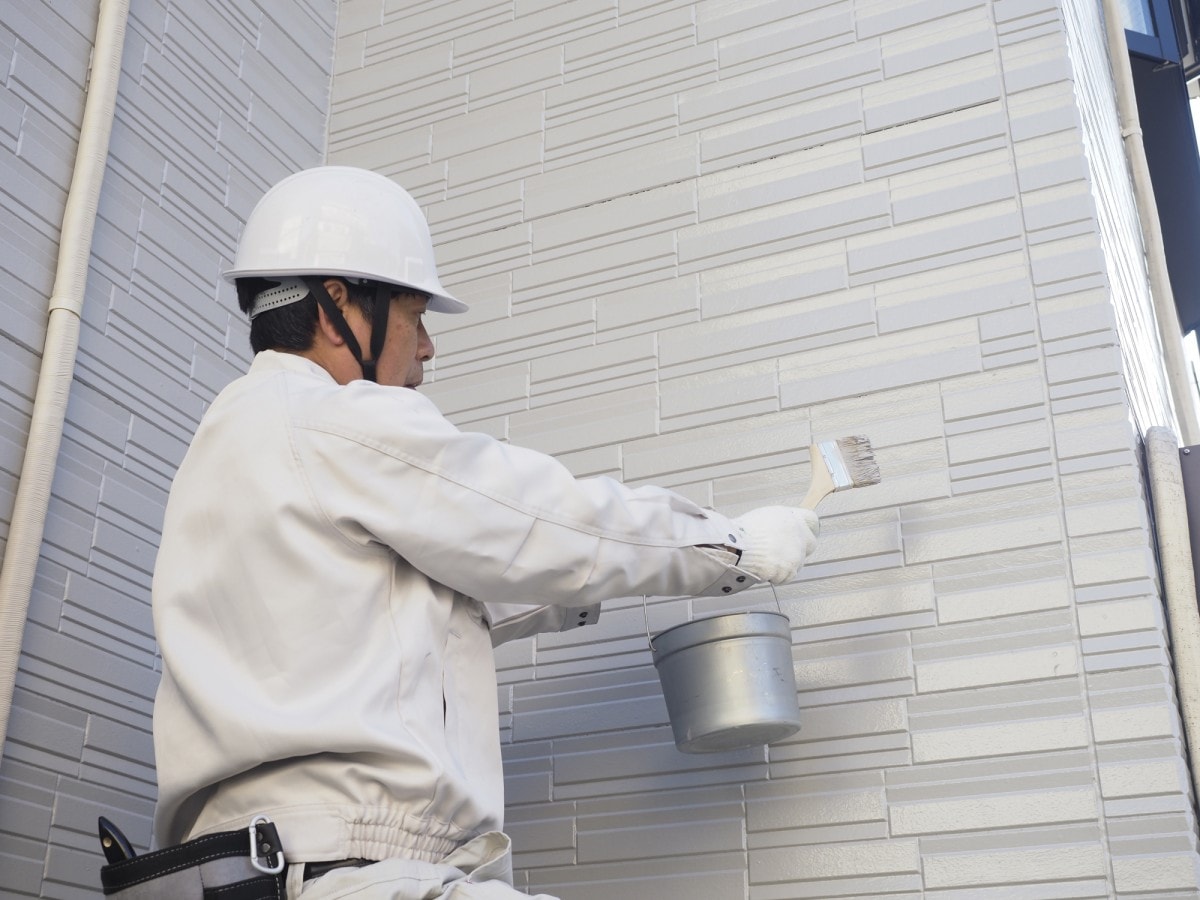 一戸建ての外壁を塗装する塗装業者の男性