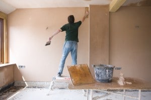 Man on step stool plastering wall in house under construction