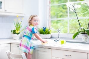 Cute curly toddler girl in a colorful dress washing dishes and p