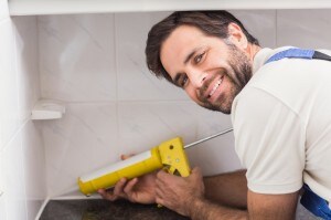 Plumber putting filling in between tiles in the kitchen