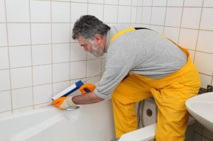 Worker caulking bath tube and tiles