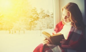 happy girl reading book by the window in winter