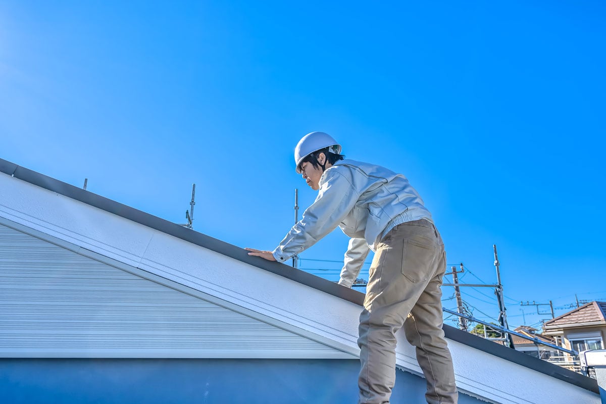 足場にのぼり住宅の屋根を点検する男性